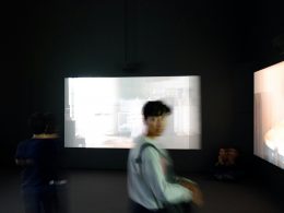 person-im-grauen-pullover-steht-vor-grossen-monitoren-dbOaUuoPXhY