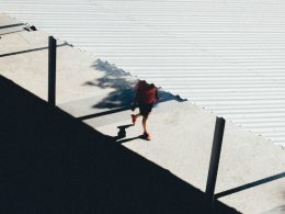 person-in-roter-jacke-und-schwarzer-hose-geht-auf-grauem-betonpflaster-in-der-nahe-eines-gewassers-COYUdbaaeQ8