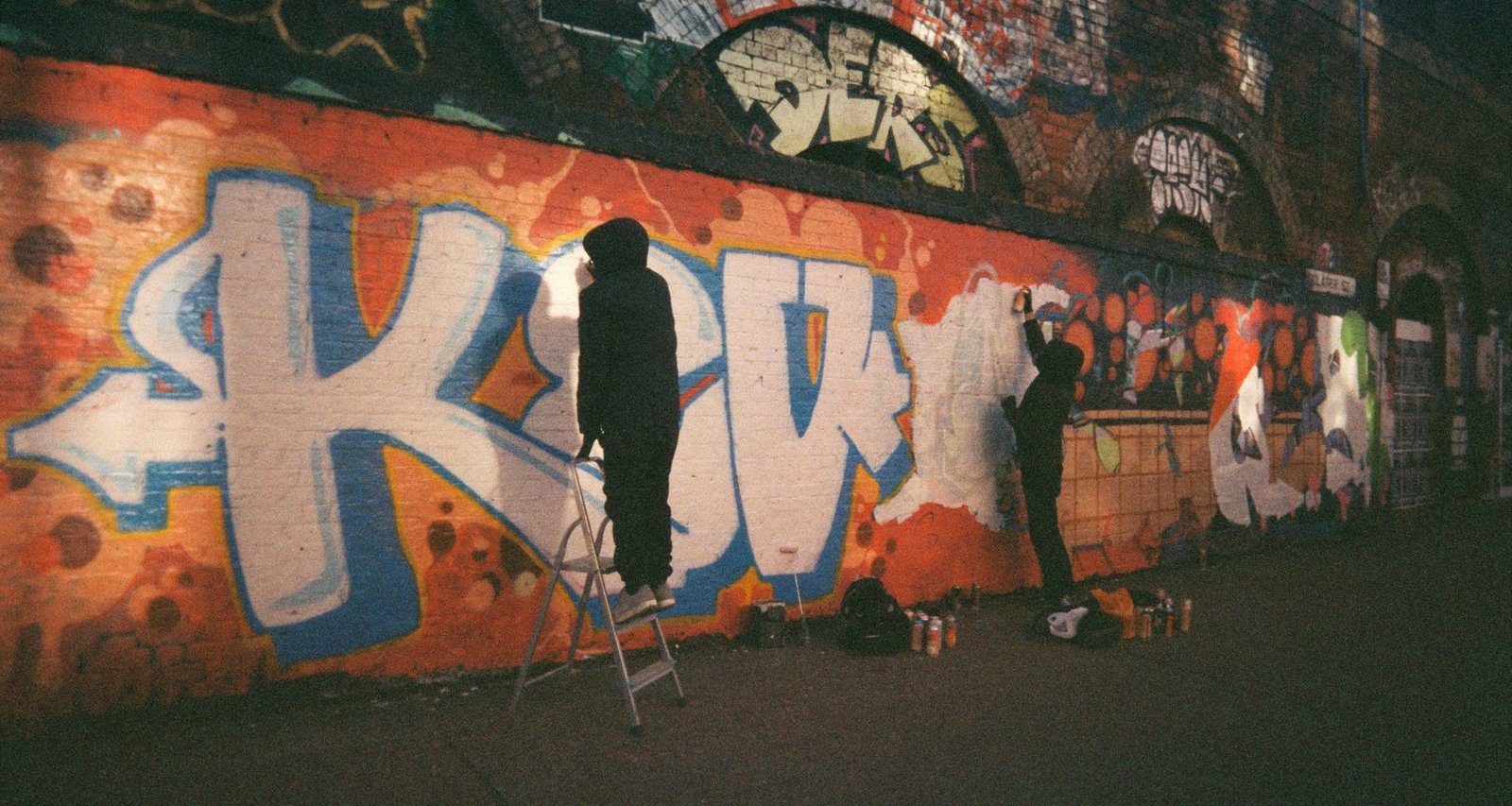 zwei-manner-malen-graffiti-an-eine-wand-kZ6WlgjZESs
