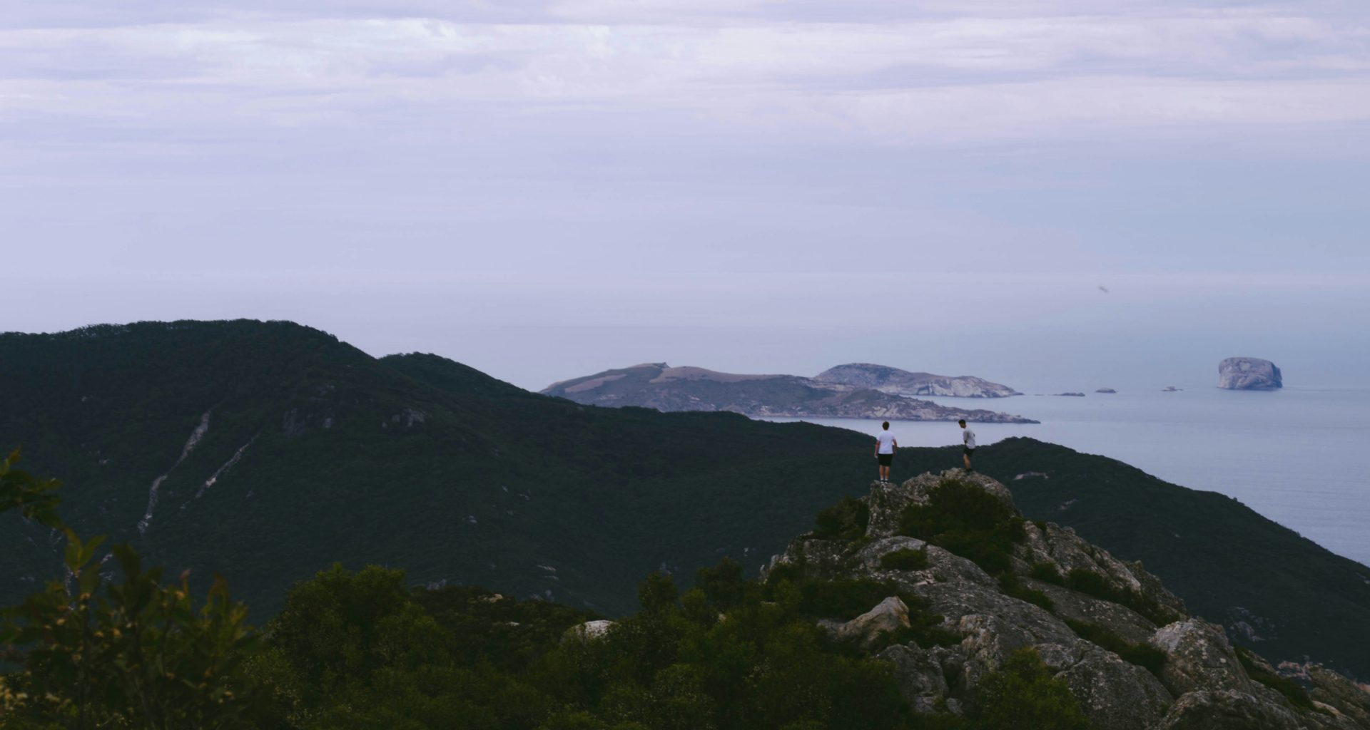 zwei-manner-stehen-auf-dem-gipfel-eines-berges-in-der-nahe-des-meeres-Lq-3swjHIl4
