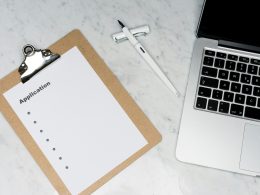 weisses-papier-auf-brauner-mappe-neben-silbernem-laptop-3Rn2EjoAC1g