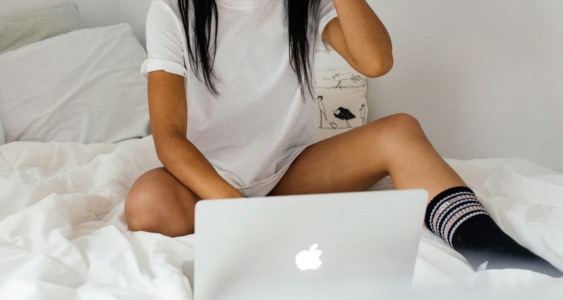 frau-tragt-weisses-t-shirt-mit-rundhalsausschnitt-auf-dem-bett-und-halt-silbernes-macbook-in-der-hand-vKEwDELlFbg