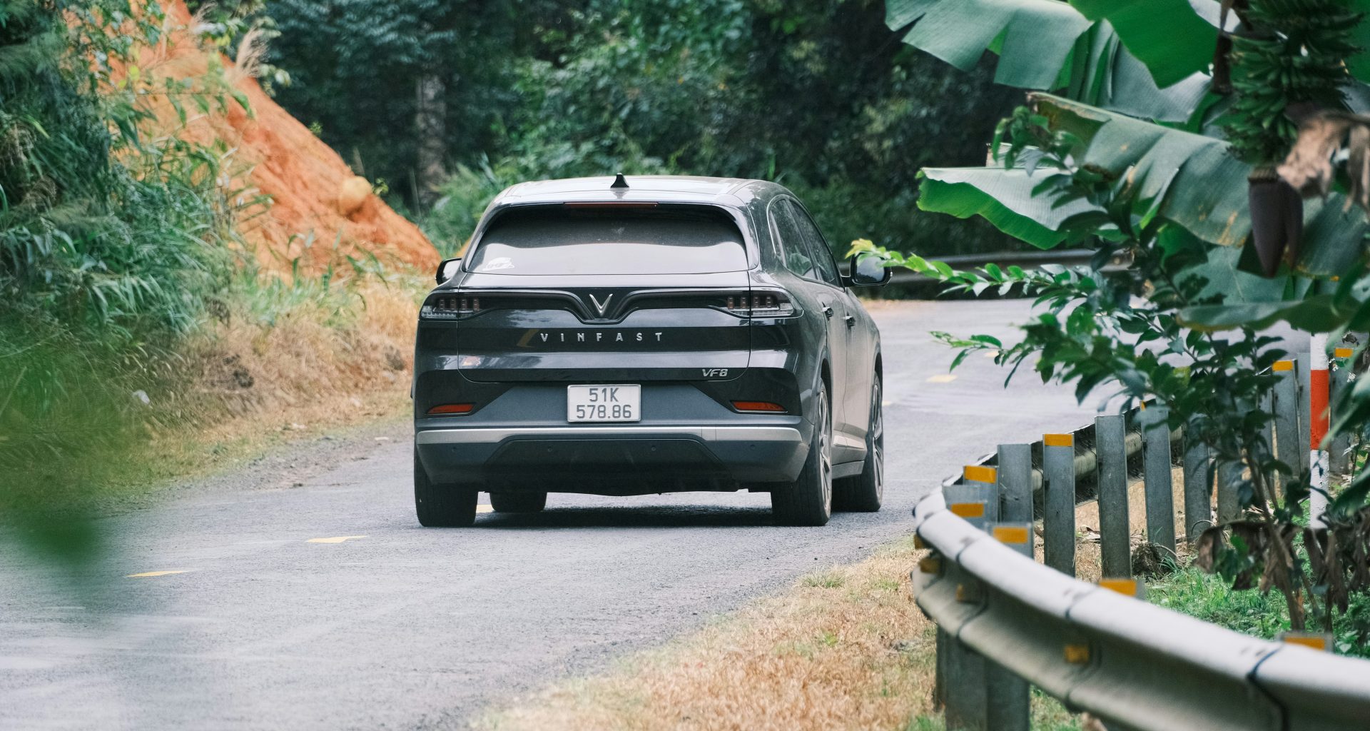 ein-schwarzes-auto-das-eine-strasse-neben-einem-uppig-grunen-wald-entlangfahrt-MB4Qh70P2RM