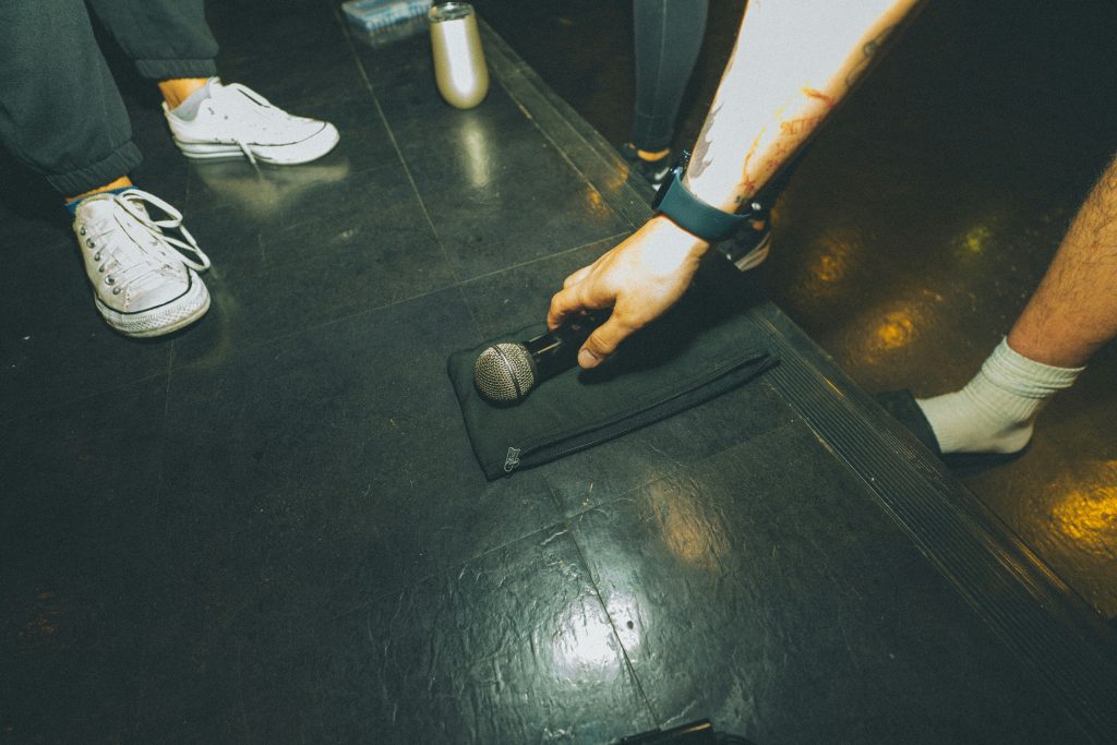 eine-person-die-ein-mikrofon-auf-einem-schwarzen-boden-halt-Ngl4R1V8ByE