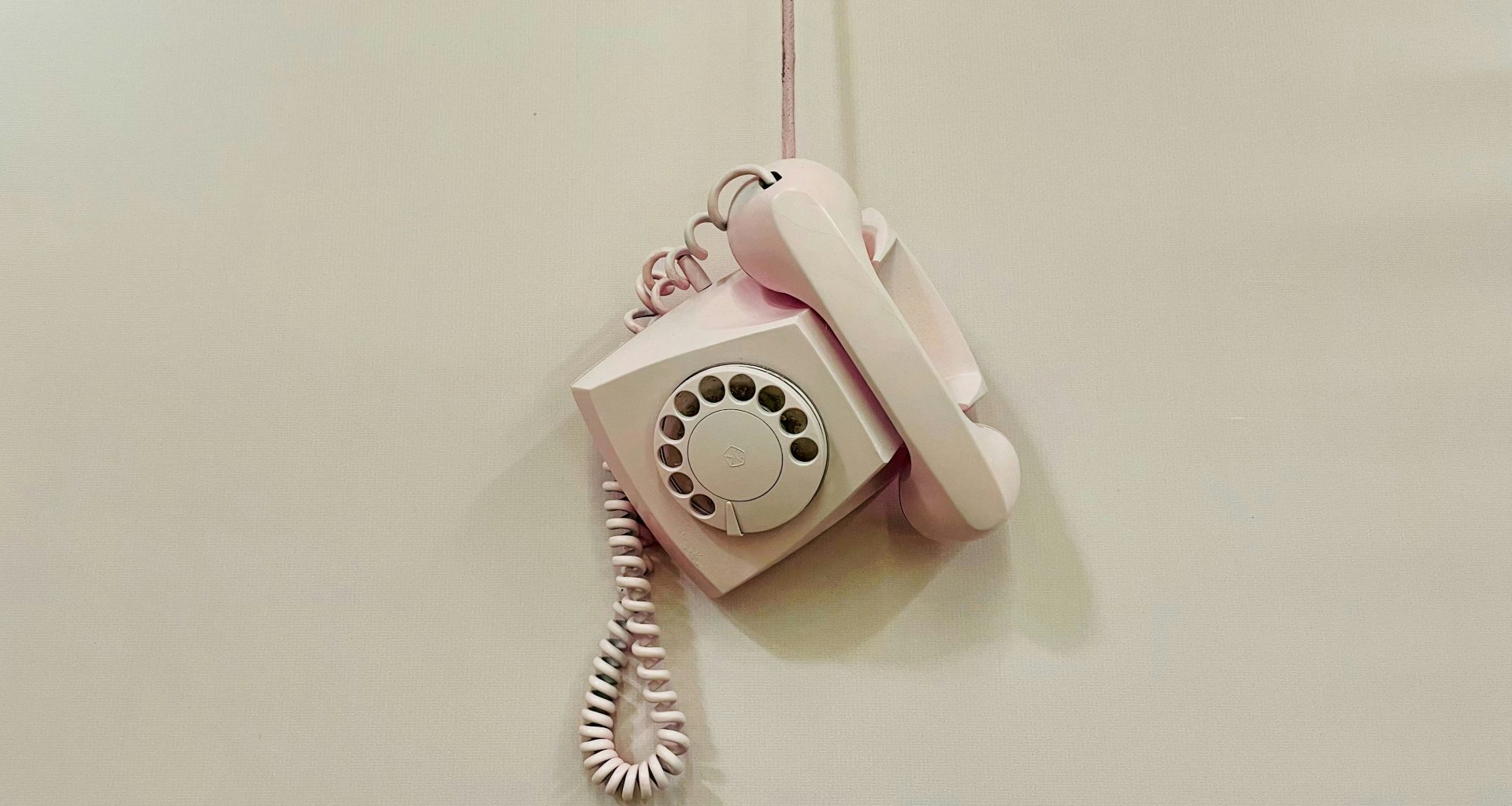 ein-rosafarbenes-telefon-das-an-einem-kabel-an-einer-wand-hangt-MwNAvpuqycc