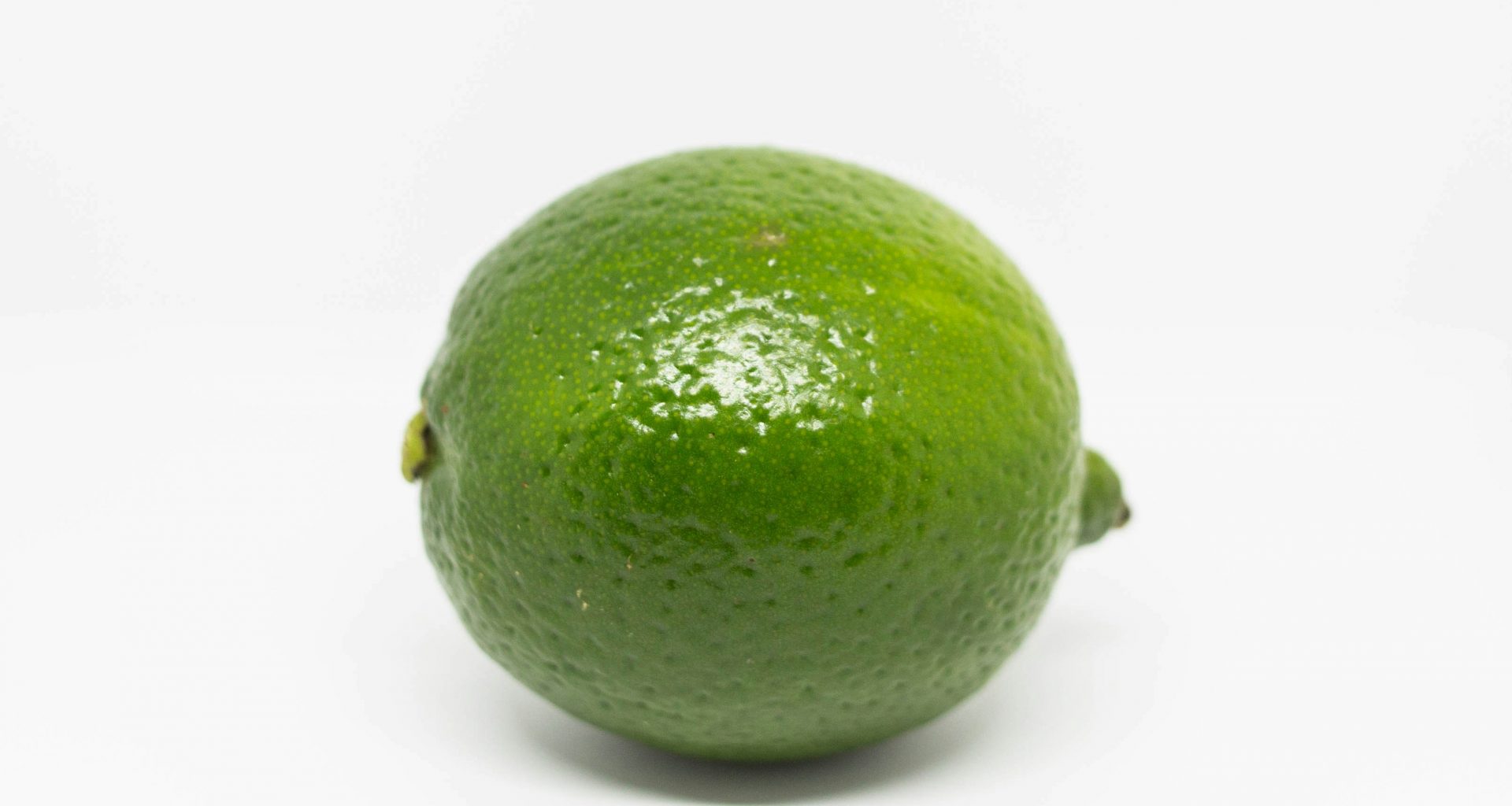 grune-limettenfrucht-auf-weisser-oberflache-ZyJ_KuMlesQ