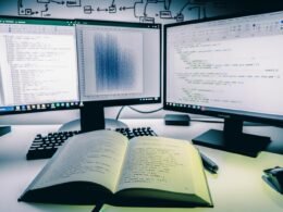 Professioneller Technik-Arbeitsplatz mit mehreren Bildschirmen, Python-Notebook mit Pandas DataFrame, Excel-Tabellen und Python-Buch mit Notizen vor kaltweißem Tageslicht.