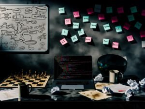 Schreibtisch im Halbdunkel mit Laptop, Python-Code, Kaffeetassen, zerknülltem Papier, Schachbrett mit KI-Symbolen, Post-its zu CI, Testing und Docs sowie Whiteboard mit komplexen Diagrammen im Hintergrund.