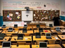 Überfüllte Schulklasse in Deutschland im Jahr 2024 mit alten Holztischen, wenigen Laptops, defektem Whiteboard und handgeschriebenen WLAN-Passwörtern an der Wand – Sinnbild für das digitale Flickwerk im deutschen Bildungssystem.