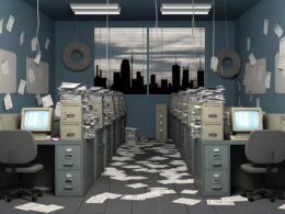 Grau-blaues, überfülltes Büro der 90er mit Aktenbergen, Papieren, alten Computern und gestressten Mitarbeitern vor einer Fensterreflexion einer modernen Stadt.