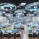 Modernes Open Space Büro mit Marketing-Analysten, die vor mehreren Screens mit Echtzeit-Daten und holografischen Diagrammen arbeiten.