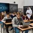 Jugendliche in einem modernen Klassenzimmer arbeiten an digitalen Geräten, ChatGPT wird auf einem großen Bildschirm angezeigt, Lehrkraft beobachtet kritisch und offen, neben Kreide und Overheadprojektor.