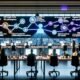 Offenes, futuristisches Büro mit multikulturellem Team, das an einem automatisierten AI-Content-Produktionsprozess arbeitet. Auf Großbildschirmen sind dynamische Workflows mit GPT-4, Claude, Gemini, Automatisierungen, SEO- und QA-Dashboards sowie KI-generierte Medieninhalte zu sehen.