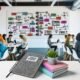 Junge Kreative arbeiten an Laptops und großen Monitoren mit bunten Content-Strategie-Diagrammen, strukturierten Workflows und Redaktionsplänen in einem modernen Büro.