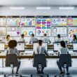 Modernes Büro mit großen Schreibtischen, mehreren Bildschirmen mit Content Creation Plattform und Team bei gemeinsamer Arbeit, digitale Whiteboards im Hintergrund.