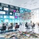 Marketer arbeiten gemeinsam in einem hellen, modernen Büro an einer digitalen Marketing-Schaltzentrale mit Echtzeit-Analytics, Automatisierung und KI-Tools, während veraltete Notizzettel und Excel-Tabellen im Vordergrund liegen.