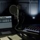 Minimalistisches Musikstudio mit Kondensatormikrofon, Audio-Interface, XLR-Kabel, Laptop mit DAW und Notizbuch vor schallabsorbierenden Wänden