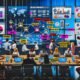 Verschiedenes Marketing-Team in modernem Büro, das an Laptops arbeitet. Im Hintergrund sind Social-Media-Dashboards, KPI-Grafiken und Influencer-Profile auf Bildschirmen sichtbar. Mitarbeiter legen bunte Post-Its mit strategischen Begriffen auf den Tisch.
