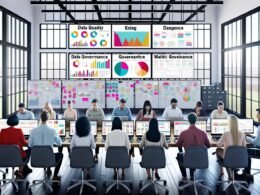 Team aus diversen Marketer:innen arbeitet konzentriert an Laptops in einem modernen Büro mit vielen Bildschirmen, Daten- und Analytics-Dashboards sowie Postern zu Data Quality und Compliance.