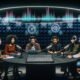Podcaster:innen mit hochwertigen Kopfhörern an einem runden Tisch, umgeben von Mikrofonen, Laptops und holographischen Audioeffekten in einem futuristischen Studio mit moderner Technologie und weicher Beleuchtung.