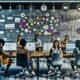 Dynamische Szene in einem modernen Social Media Büro mit mehreren Strategen, Bildschirmen voller Analysen, grafischen Tools und kollaborativem Brainstorming.