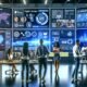 Modernes Büro mit großen Bildschirmen, die UGC-Dashboards zeigen, während Marketer und Data Scientists Diagramme und User-Content wie Selfies und Produktbewertungen analysieren.
