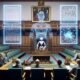 Futuristischer Sitzungssaal mit digitalen Displays, holografischem Gesetzestext, humanoidem Roboter und nachdenklichen Politikern, umgeben von klassischen Parlaments- und Staatssymbolen.