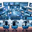 Futuristischer Arbeitsplatz mit zwei Marketern an Schreibtischen, umgeben von Monitoren mit Podcast-Marketing-Dashboards, digitalen Datenströmen und visualisierten Audio-Wellenformen.