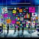 Dynamische Illustration einer Agentur: Kreatives Brainstorming mit bunten Post-its, Laptops, modernen Bildschirmen und inspirierenden Plakaten in einem urbanen, farbenfrohen Umfeld.