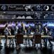 Dynamische Szene im modernen Kontrollzentrum, Analyst:innen diskutieren vor interaktiven Dashboards mit Datenvisualisierungen und KPIs.