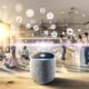 Moderne Wohnküche mit verschiedenen Personen, die smarte Lautsprecher wie Amazon Echo, Google Nest, Sonos, Apple HomePod und einen hervorgehobenen Spotify-Speaker nutzen, umgeben von futuristischen Interface-Elementen.