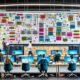 Dynamisches IT-Büro mit Dashboard, Mitarbeitenden an Laptops, Sticky Notes mit ETL und API, Whiteboard, Server-Racks und kollaborativem Workflow.