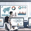 Modernes Data-Office mit zentralem Bildschirm voller klarer Diagramme, zwei Personen analysieren Visualisierungen im Vordergrund, umgeben von Monitoren mit Dashboards