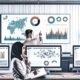 Modernes Data-Office mit zentralem Bildschirm voller klarer Diagramme, zwei Personen analysieren Visualisierungen im Vordergrund, umgeben von Monitoren mit Dashboards