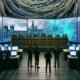 Futuristischer Serverraum mit Adern-ähnlichen Kabelbäumen, Bundestagspult, digitalen Gesetzestexten und Gruppen aus Entwicklern und Politikern vor interaktiven Bildschirmen mit GitHub-Daten.