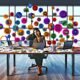 Überladener Schreibtisch mit verstreuten Marketingdaten, gestresstem Marketer und schwebenden Symbolen für verschiedene Marketing-Tools in einem modernen Büro.