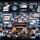 Digitale Redaktion im Loft-Stil mit großen Monitoren, Team bei der Entwicklung von Post-Paywall-Strategien, Datenvisualisierungen, Community-Features und Social-Media-Icons.