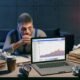 Gestresster Blogger blickt spätabends auf leere Google Analytics-Daten am Laptop, umgeben von Kaffeetassen, zerknüllten Notizen und SEO-Büchern auf einem unordentlichen Schreibtisch.