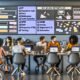 Junges, diverses Team brainstormt im Hightech-Büro für eine Newsletter-Kampagne. Große Checkliste am Monitor, moderne Geräte, offene Laptops und bunte Analysediagramme vermitteln einen dynamischen, fokussierten Arbeitsalltag im Jahr 2025.