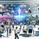 Modernes, diverses Kreativteam arbeitet dynamisch in einem offenen Workspace mit digitalen Tools, Tech-Gadgets, großen Screens, KI-generierten Bildern und futuristischen Interfaces, im Hintergrund ein digital vernetztes Großstadtpanorama.