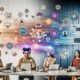 Vielfältiges Team arbeitet vor Laptops, digitalen Whiteboards mit KI-Mindmaps, API-Integrationen und schwebenden AR-Grafiken in einem visionären, vernetzten Workspace