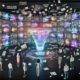 Futuristisches Büro mit transparenten Displays, KI-gesteuerten Werbekampagnen, einem holographischen Assistenten und kreativen Teams in lebendiger Arbeitsatmosphäre.