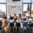 Junges, diverses SEO-Team arbeitet gemeinsam im modernen Loft-Büro in Dresden, umgeben von Laptops, Notizbüchern und Whiteboard mit SEO-Strategie-Skizzen, im Hintergrund die Dresdner Neustadt und Frauenkirche.
