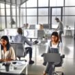 Modernes, minimalistisches Agentur-Büro mit Glaswänden und offenem Workspace, in dem ein diverses SEO-Team an Computern mit Dashboards und Code arbeitet.