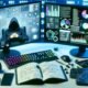 Technisch moderner Arbeitsplatz mit ultrabreiten Monitoren voller Daten, Charts und Dashboards, daneben Notizbuch, Tastatur, Maus, Smartphone und Headset, im Hintergrund digitale Zahlen und Codezeilen.