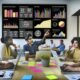 Marketingteam im modernen Büro, das vor einem großen Bildschirm mit anschaulichem Daten-Dashboard zusammenarbeitet und Datenanalysen diskutiert