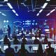 Gruppe junger Marketingexperten in einem modernen Großraumbüro, umgeben von Monitoren mit Statistik-Dashboards, Prozessdiagrammen und digitaler Ausstattung.
