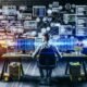 Illustration eines jungen Entrepreneurs in einem urbanen Loft, am Schreibtisch mit Monitoren voller Dashboards und Code, umgeben von digitalen Symbolen, Whiteboards und Post-Its mit Technologie-Stichworten.