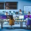 Fokussiertes TYPO3 SEO-Team aus Entwicklern, SEOs und Designern an einer großen Workstation, umgeben von Monitoren mit Code, Analytics und TYPO3-Backend, mit Whiteboard und Fachbegriffen im Hintergrund