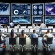 Modernes E-Commerce-Kontrollzentrum mit Analysten vor großen Bildschirmen, die komplexe Live-Daten und KPIs überwachen. Im Hintergrund leuchten Serverracks und Hologramme zeigen vernetzte Datenströme.